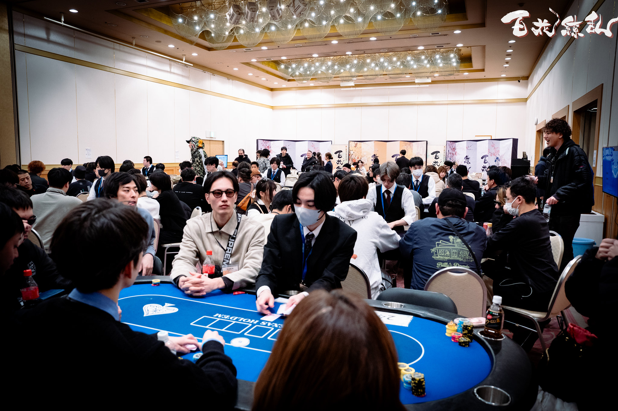 複数のポーカーテーブルと多くの参加者でにぎわう百花繚乱の会場全景